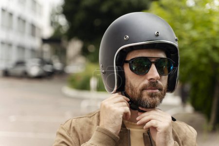Téléchargez les photos : Portrait rapproché d'un beau motard sérieux portant un casque de moto et des lunettes de soleil élégantes prêtes à rouler en moto. Aventure, liberté, concept de road trip - en image libre de droit