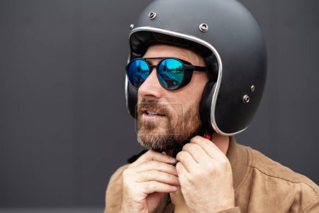 Foto de Guapo barbudo ciclista con casco de motocicleta y gafas de sol elegantes listo para montar en moto. Aventura, libertad, concepto de viaje por carretera - Imagen libre de derechos
