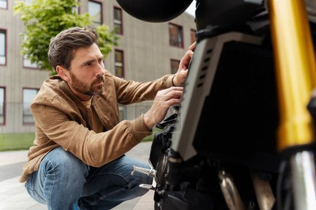 Téléchargez les photos : Homme barbu fort motard répare sa moto dans la rue. Mécanicien de fixation moto seul. Formation professionnelle, réparation du concept de moto - en image libre de droit
