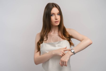 Photo for Portrait of busy woman checking time, wearing dress, long beautiful hair, looking at camera. Attractive successful girl waiting isolated on gray background. ?oncept of shopping, natural beauty - Royalty Free Image
