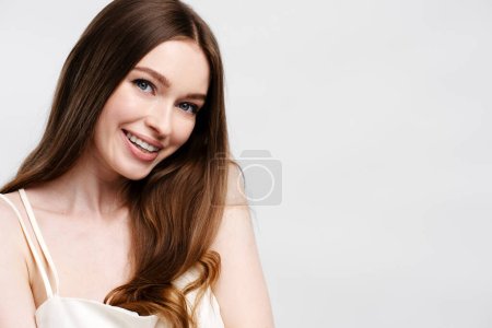 Foto de Retrato de una hermosa mujer sonriente con el pelo largo con camisón mirando a la cámara. Elegante hembra posando aislada sobre fondo gris. Concepto de cuidado del cabello, espacio de copia - Imagen libre de derechos