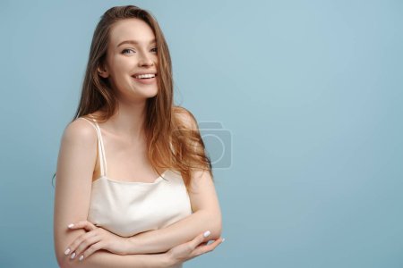 Foto de Retrato de una hermosa mujer sonriente con el pelo largo y saludable, sonrisa dentada mirando a la cámara aislada sobre fondo azul. Belleza natural, concepto de cuidado de la piel - Imagen libre de derechos