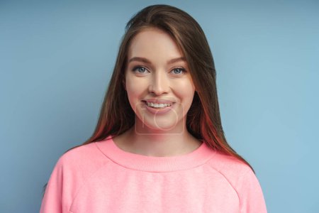 Téléchargez les photos : Gros plan portrait d'une belle femme souriante avec un sourire de dents regardant la caméra après la procédure dentaire. Modèle attrayant avec maquillage naturel sur le visage isolé sur fond rose - en image libre de droit