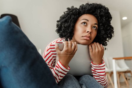 Téléchargez les photos : Triste femme afro-américaine fatiguée tenant un ordinateur portable assis seul à la maison, se sentant malheureuse. Dépression - en image libre de droit