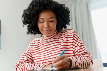 Photo for Smiling African American woman, writer taking notes. Smart student studying, learning language - Royalty Free Image