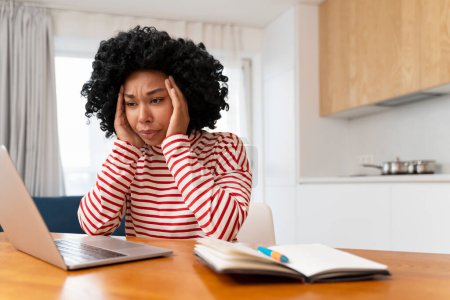Téléchargez les photos : Femme afro-américaine fatiguée frustrée utilisant un ordinateur portable travaillant en ligne à partir de la maison. Mal de tête, stress - en image libre de droit