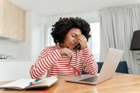 Téléchargez les photos : Fatiguée femme afro-américaine frustrée travaillant en ligne de la maison ayant des douleurs oculaires. Mal de tête, stress - en image libre de droit