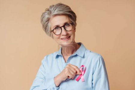 Foto de Mujer mayor confiada sosteniendo cinta rosa aislada en el fondo. Mes de sensibilización sobre el cáncer de mama - Imagen libre de derechos