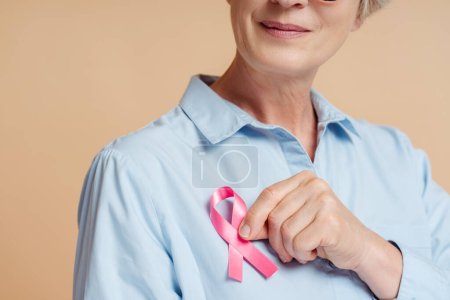 Senior Frau mit rosa Schleife isoliert auf dem Hintergrund. Konzept zur Sensibilisierung für Brustkrebs