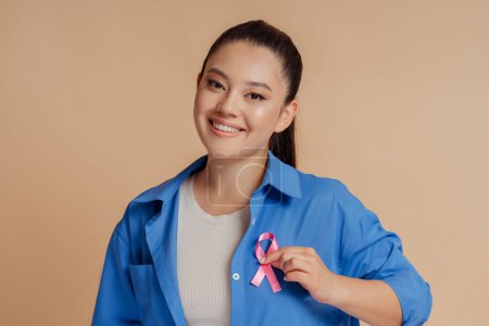 Foto de Mujer asiática sonriente con cinta rosa aislada sobre fondo. Concepto mensual de concienciación sobre el cáncer de mama - Imagen libre de derechos