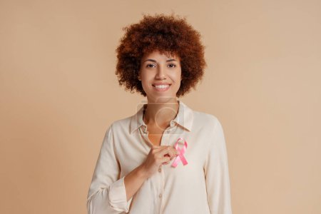 Foto de Mujer afroamericana sosteniendo cinta rosa aislada en el fondo. Mes de sensibilización sobre el cáncer de mama - Imagen libre de derechos