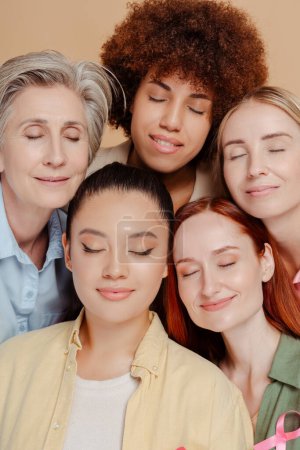 Foto de Rostros multiétnicos de mujeres con los ojos cerrados usando cinta rosa de cáncer de mama aislada en el fondo - Imagen libre de derechos