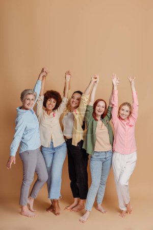 Foto de Las mujeres multiétnicas que usan cinta rosa levantando las manos celebran la recuperación. Concientización sobre el cáncer de mama - Imagen libre de derechos