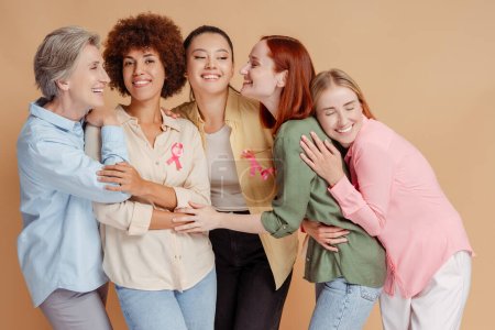 Photo for Group of smiling women wIth breast cancer pink ribbon hugging, support each other isolated - Royalty Free Image