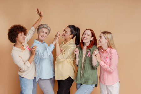 Foto de Las mujeres emocionales que usan cinta rosa levantando las manos celebran la recuperación. Mes de sensibilización sobre el cáncer de mama - Imagen libre de derechos