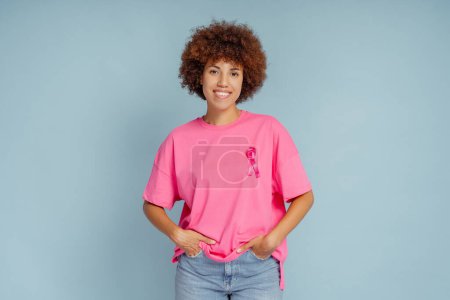 Foto de Mujer afroamericana con cinta rosa aislada sobre fondo azul. Mes de sensibilización sobre el cáncer de mama - Imagen libre de derechos