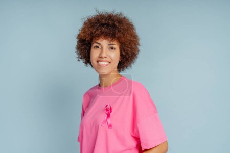 Foto de Mujer afroamericana sonriente con fondo aislado de cinta rosa. Mes de sensibilización sobre el cáncer de mama - Imagen libre de derechos