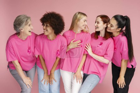 Téléchargez les photos : Femmes souriantes multiethniques en t-shirts avec ruban rose communication isolé sur fond rose - en image libre de droit