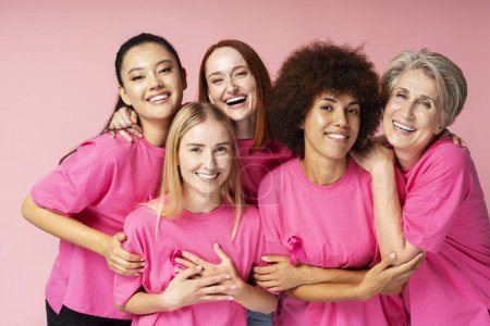 Téléchargez les photos : Femmes portant des t-shirts avec ruban rose isolé sur fond rose. Mois de sensibilisation au cancer du sein - en image libre de droit