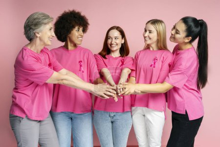 Photo for Smiling women with breast cancer pink ribbon holding hands together isolated on pink background - Royalty Free Image