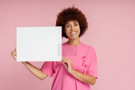 Foto de Mujeres afroamericanas sonrientes con cáncer de mama cinta rosa sosteniendo pancarta vacía aislada, maqueta - Imagen libre de derechos