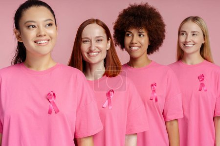Foto de Mujeres sonrientes multirraciales con cinta rosa aislada sobre fondo rosa. Concientización sobre el cáncer de mama - Imagen libre de derechos