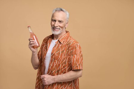 Foto de Caucásico de pelo gris barbudo guapo hombre mayor en las vacaciones de verano, sosteniendo una refrescante limonada, sonriendo mirando a la cámara, aislado sobre fondo beige. Copia el espacio publicitario. Viajar. Turismo. Gente - Imagen libre de derechos