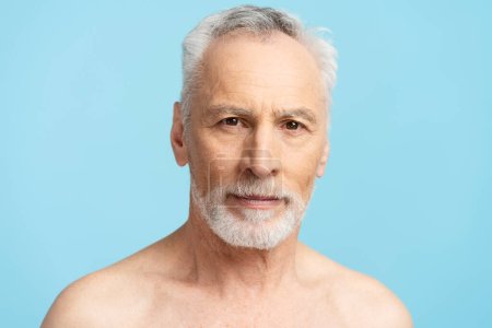 Téléchargez les photos : Portrait rapproché d'un vieil homme pensif isolé sur fond bleu. Attrayant mâle mature, concept de soins du corps, procédures de beauté - en image libre de droit