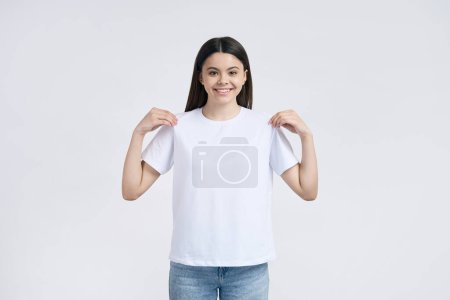 Photo for Teenage girl smiling with a beautiful toothy smile, looking confidently at camera, wearing a white casual blank t-shirt with mockup, template, copy space for advertising text, isolated background - Royalty Free Image
