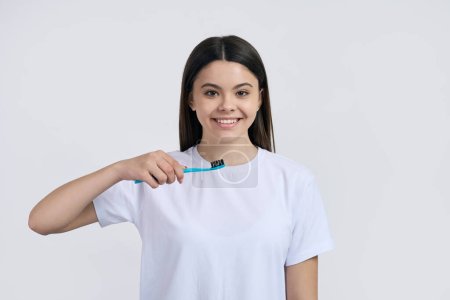Photo for Lovely Caucasian teenage girl in white casual t-shirt, holding a toothbrush, isolated on white studio background. Healthcare and medicine. Tooth care concept. Pediatric dentistry. Oral care - Royalty Free Image