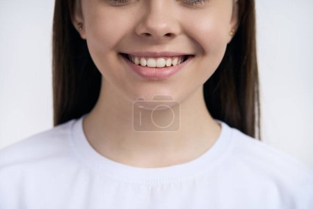 Foto de Vista recortada de la cara de una adolescente en camiseta blanca, sonriendo con una hermosa sonrisa dentada, aislada sobre fondo blanco. Concepto de cuidado dental e higiene bucal. Cuidado dental. Odontología estética - Imagen libre de derechos
