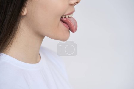 Téléchargez les photos : Vue dégagée. Portrait latéral d'une adolescente montrant la langue et des dents blanches propres parfaites, isolées sur fond blanc. Soins dentaires et concept d'hygiène buccodentaire. Soin des dents. Dentisterie esthétique - en image libre de droit
