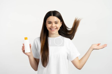 Foto de Hermosa chica adolescente sonriente con cabello largo sosteniendo champú aislado sobre fondo blanco. Concepto de cuidado del cabello - Imagen libre de derechos