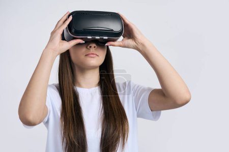 Foto de Close-up chica adolescente con casco de realidad virtual auriculares sobre fondo blanco aislado. Adolescente experimentando realidad virtual con gafas VR. Tecnología, innovación, simulación, concepto de videojuegos - Imagen libre de derechos