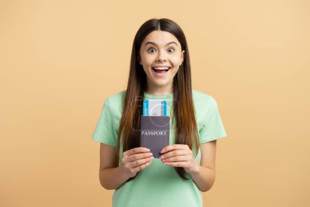 Téléchargez les photos : Portrait d'une jeune adolescente heureuse tenant un passeport et une carte d'embarquement isolés sur fond beige. Concept de voyage - en image libre de droit