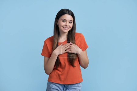 Photo for Lovely girl putting her hands over her heart, smiling with a cute toothy smile looking at camera, showing you her sympathy and love, standing isolated over blue background. People. Gestures. Emotions - Royalty Free Image