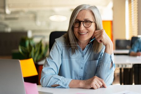 Photo for Portrait of smiling confident senior businesswoman, real estate agent, looking at camera in modern office. Gray haired manager wearing stylish eyeglasses sitting at workplace. Successful business - Royalty Free Image