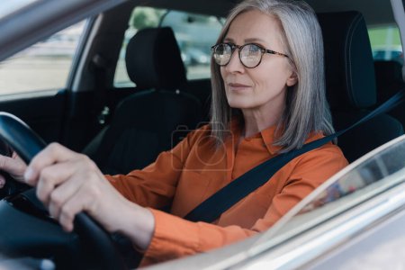 Beautiful confident senior woman driving new car. Road trip, transportation concept
