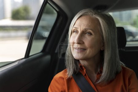 Photo for Portrait of smiling successful senior woman looking at window sitting inside taxi, copy space. Transportation concept - Royalty Free Image