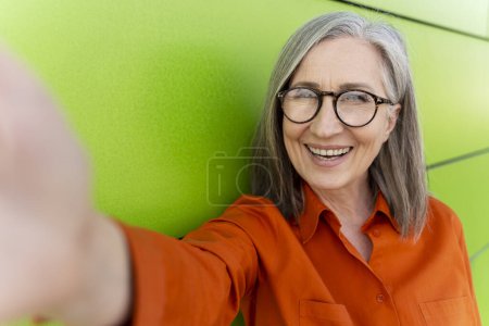 Foto de Confiado sonriente mujer madura de pelo gris tomando selfie, comunicación en línea, tener videollamada de pie al aire libre. Concepto tecnológico - Imagen libre de derechos