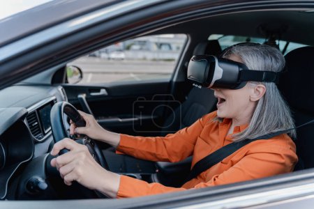 Photo for Overjoyed senior woman wearing virtual reality glasses, driving car with open mouth. Transportation, modern technology concept - Royalty Free Image