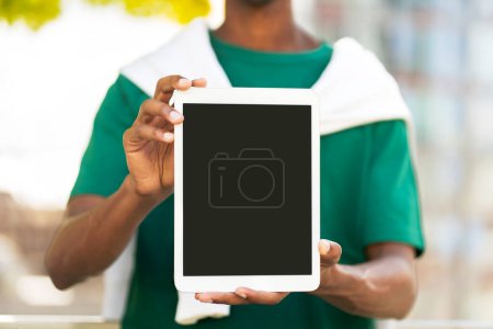 Téléchargez les photos : Jeune homme en vêtements décontractés tenant tablette numérique avec écran blanc, place pour la publicité, maquette à l'extérieur, dans le parc. Concept de publicité - en image libre de droit
