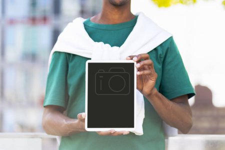 Téléchargez les photos : Jeune homme en vêtements décontractés tenant tablette numérique avec écran blanc, place pour les annonces, maquettes à l'extérieur, dans le parc. Concept de publicité - en image libre de droit