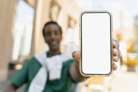 Téléchargez les photos : Homme afro-américain souriant montrant écran blanc vierge de téléphone portable, maquette, endroit pour le texte. Concept technologique - en image libre de droit