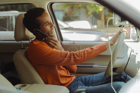 Foto de Retrato de un hombre afroamericano guapo sonriente conduciendo un coche, hablando por teléfono móvil, respondiendo a una llamada. Concepto de comunicación - Imagen libre de derechos