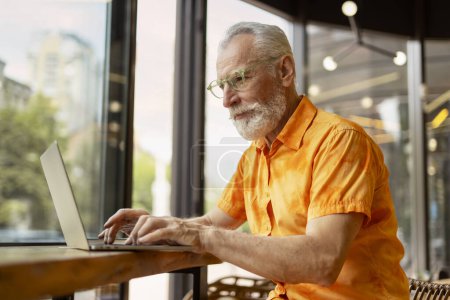 Téléchargez les photos : Beau senior homme, programmeur utilisant un ordinateur portable travaillant en ligne assis dans un café moderne. Homme d'affaires élégant planification démarrage, la recherche d'informations sur le site. Concept d'entreprise réussi - en image libre de droit