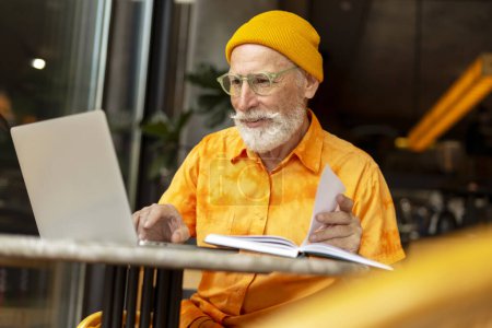 Beau senior homme, programmeur utilisant un ordinateur portable travaillant en ligne assis dans un café moderne. Étudiant âgé élégant étudiant, apprentissage de la langue, recherche d'informations, concept d'éducation en ligne 