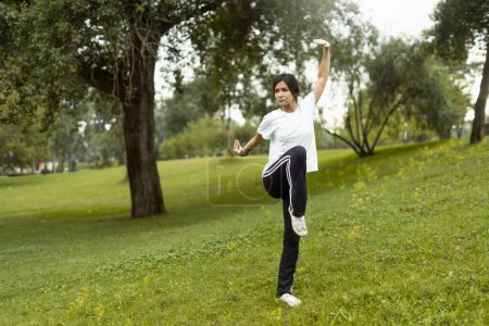 Téléchargez les photos : Portrait de femme sérieuse portant un entraînement de vêtements de sport, pratiquant le wushu dans le parc. Style de vie sain, kungfu, concept d'arts martiaux - en image libre de droit