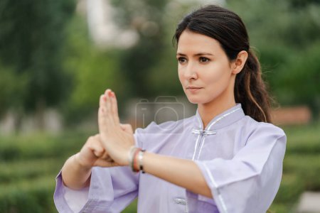 Photo for Focused wushu woman training balance and standing in special pose while exercising at green summer park. Healthcare practices concept - Royalty Free Image