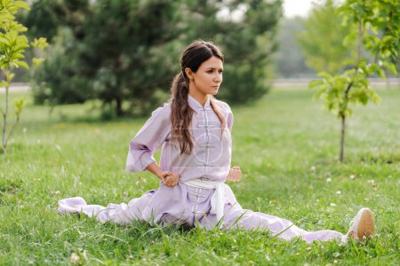 Photo for Portrait of serious woman wearing kimono sitting at the twine, practicing wushu in park. Healthy lifestyle, kungfu, martial arts concept - Royalty Free Image